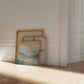 Framed artwork leaning against a wall in a room with wooden flooring.