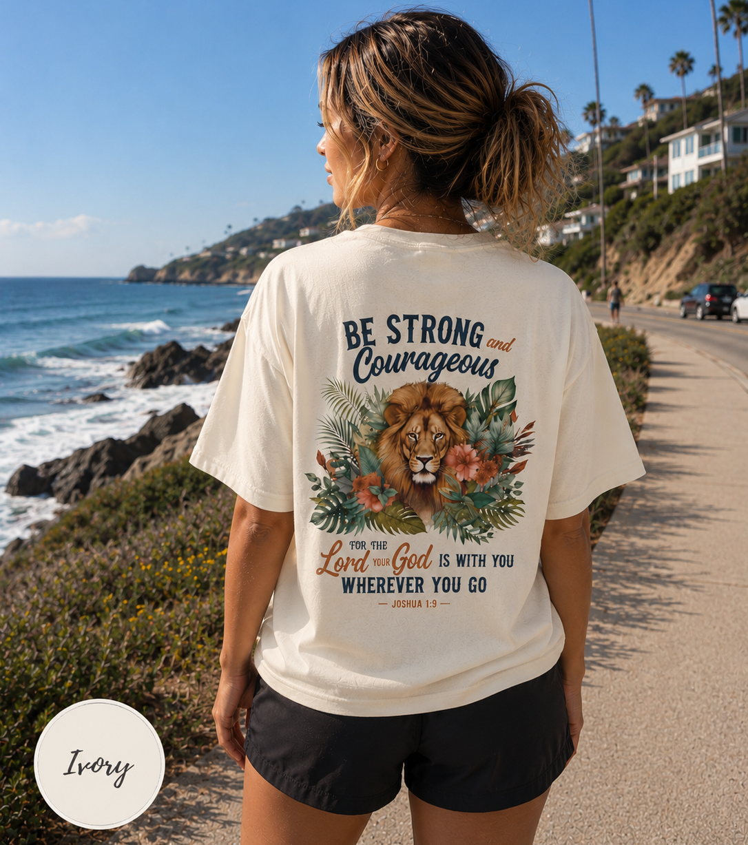 Woman wearing a t-shirt with a Bible verse and lion of Judah by the ocean.