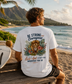 Man sitting on a beach with a scenic view, wearing a white t-shirt with a motivational quote and lion graphic.