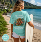 Woman on a beach holding a surfboard wearing a teal t-shirt with lion of Judah Bible surf shirt