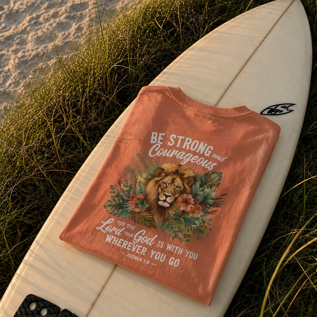 Orange t-shirt with motivational quote and lion graphic on a white surfboard by the water