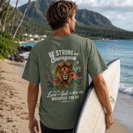 Man holding a surfboard on a beach with a scenic background, wearing a Christian t-shirt with a motivational design.